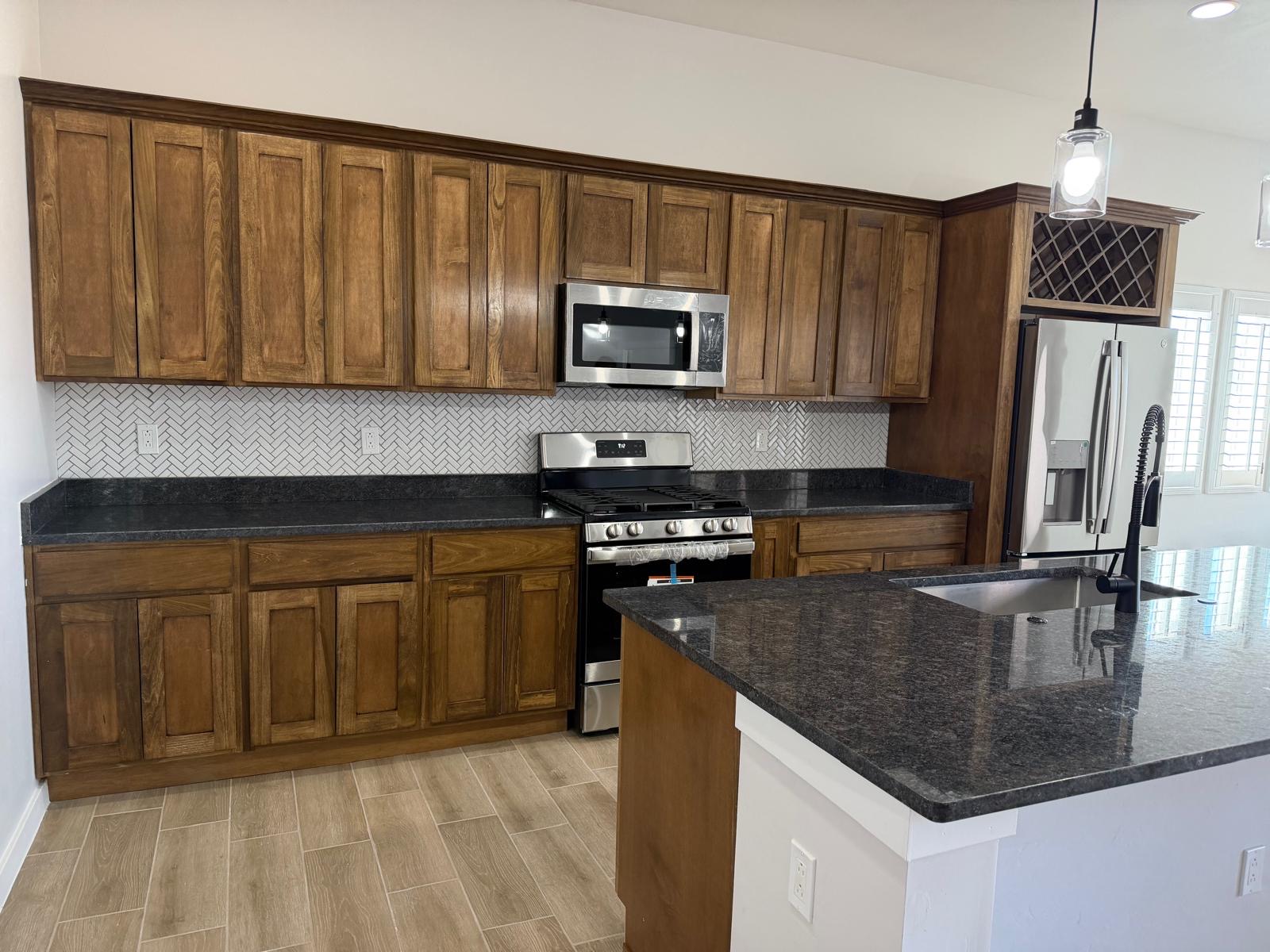 Stained wood kitchen cabinets with granite countertops and herringbone backsplash